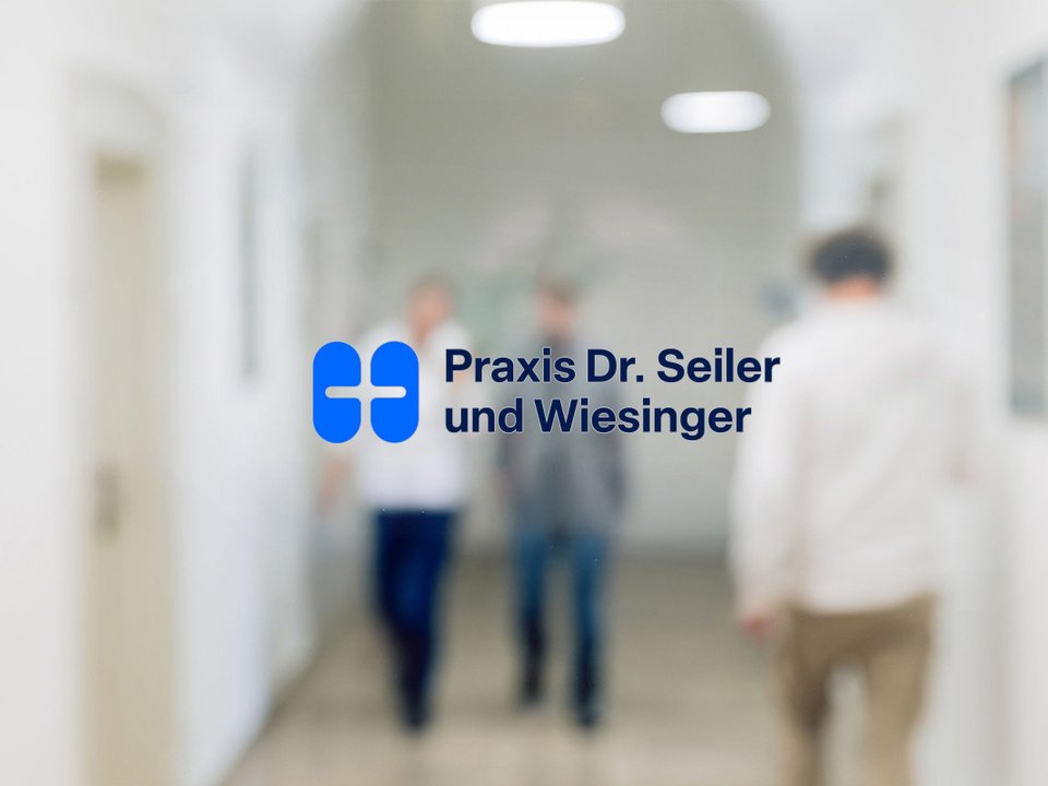 Blick durch die Glastür mit Praxislogo auf den Flur, durch den Mitarbeitende und Patient laufen.