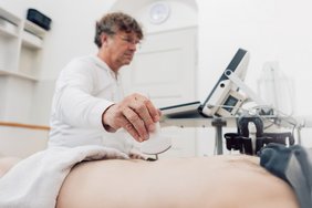 Ein Arzt führt eine Ultraschalluntersuchung durch und setzt den Schallkopf an; daneben steht das Ultraschallgerät.